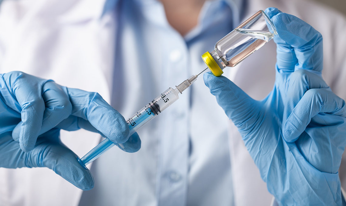 hands holding a syringe and vaccine vial